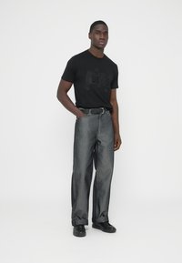 Czarna koszulka z krótkim rękawem z subtelnym nadrukiem logo, zestawiona z luźnymi, spranymi szarymi dżinsami i czarnymi butami. Prosty, nowoczesny strój.