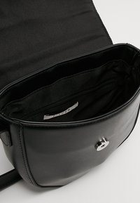 Borsa nera in ecopelle con chiusura a scatto magnetica, tasca interna con zip e fodera in tessuto morbido. Design semplice e arrotondato.