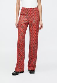 Røde mønstrede bukser med diamantdesign, en udvidet pasform og en glat tekstur, kombineret med sorte flade sko.
