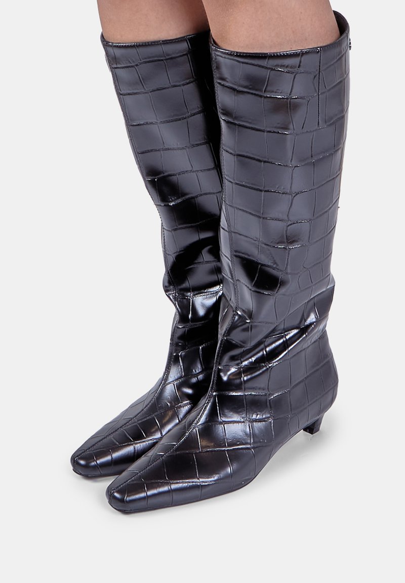 Botine negre, până la genunchi, din material lucios, matlasat, cu vârf ascuțit și toc mic. Prezintă un model texturat în grilă și un fermoar.