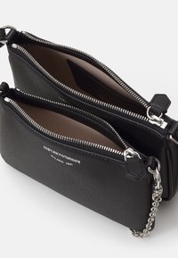 Černá texturovaná kožená crossbody taška se dvěma zipovými přihrádkami, stříbrným kováním a řetízkem; na přední straně se nachází logo značky.
