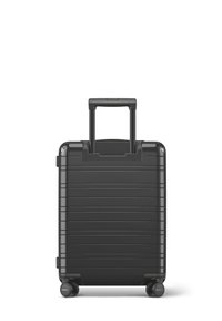 Valise noire rigide avec une poignée rétractable et quatre roues, présentant un design rainuré pour la texture et la durabilité.