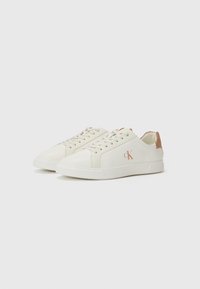 Sneakers bianchi in pelle con finitura liscia, caratterizzati da un accento beige sul tallone e un logo sottile sul lato. Design con lacci.