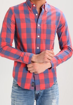 Mand iført rød og blå ternet skjorte med brystlomme, der justerer ærmet over falmede, revnede blå jeans.
