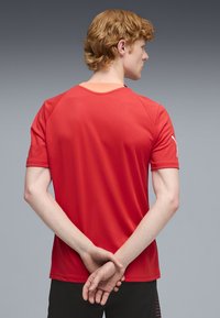 Camiseta deportiva roja de manga corta, con cuello redondo y textura suave. Vista trasera muestra un diseño simple sin patrones visibles.