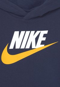 Sudadera azul marino con un gran logotipo blanco de "NIKE" y un gráfico de swoosh amarillo. Material de algodón con una textura suave y un bolsillo tipo canguro en la parte delantera.