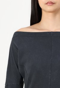 Tmavě námořnický off-the-shoulder top vyrobený z jemné látky, s volným střihem, širokým výstřihem a jemnou texturou s viditelnými švy.