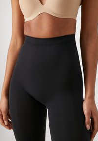 High-waisted black leggings made of smooth, elastic material, featuring a seamless waistband for comfort and a fitted silhouette.