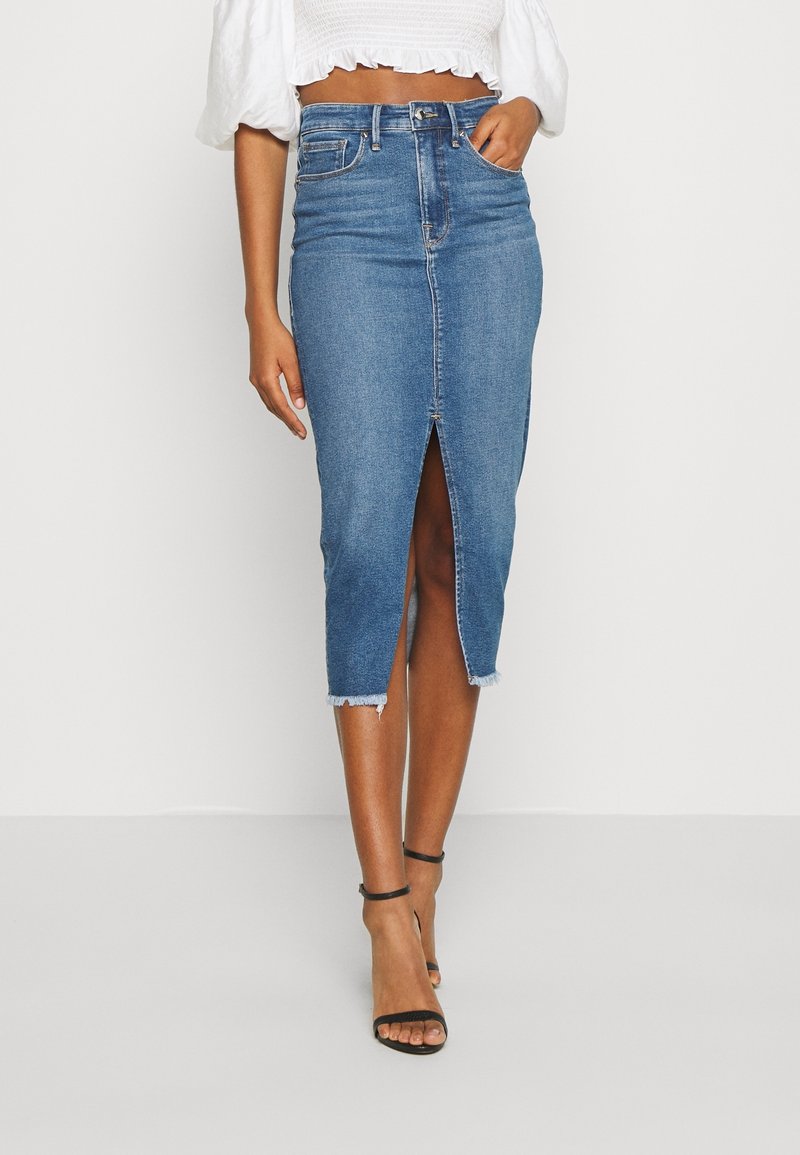 Farkkuhame keskipitkällä leikkauksella, jossa etuslitsi, viimeistelemätön helma ja klassinen sininen väri. Yhdistetty valkoiseen lyhytpaitaiseen toppiin ja mustiin korkokenkiin.