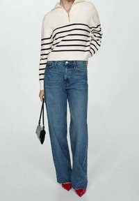 Gestreepte gebreide trui in crème en zwart, met een half-ritsontwerp; high-waisted blauwe jeans; zwarte handtas; rode puntige hakken; comfortabele pasvorm.