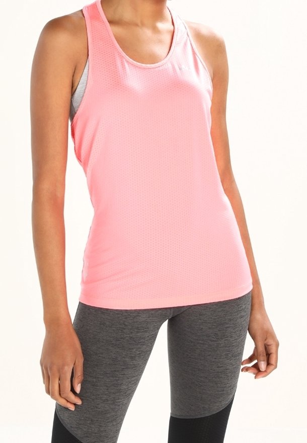 Kobieta w bezrękawnikowej różowej koszulce sportowej i szarych legginsach stoi na tle jednolitego tła.