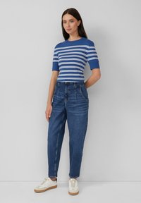 Top a maniche corte a righe blu abbinato a jeans blu a vita alta e sneakers bianche, su uno sfondo chiaro e semplice.