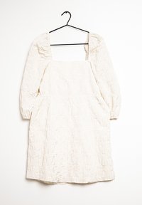 Valkoinen rypistyvä mekko, jossa on neliömäinen pääntie, puffihihat ja elastiset hihansuut, roikkumassa mustalta koukulta valkoista taustaa vasten.