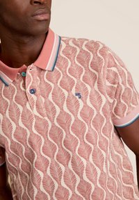 Korte mouw polo-shirt in koraal met golfpatroon, crèmekleurige achtergrond, contrasterende kraag en knopen, en subtiele logodetail.