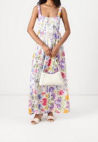 Maxiklänning med blommönster i olika färger, med fyrkantig halsringning och tjocka band. I sällskap med en vit handväska med snörningsdetaljer.
