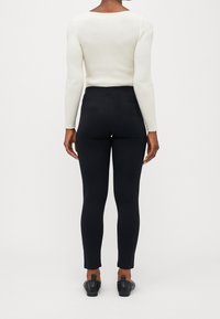 Svarta leggings med hög midja, kombinerade med en krämfärgad ribbad långärmad topp. Tyget verkar slätt och figurnära.
