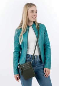 Turquoise leather jacket with a zip front, side pockets, and textured finish. Paired with a dark green crossbody bag featuring multiple zippers.