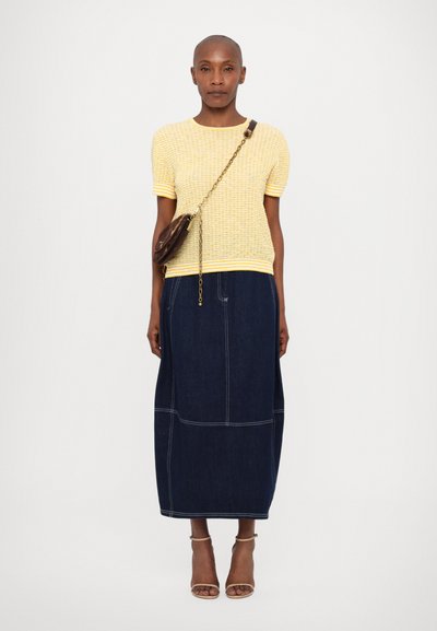 Gulstribet strikket kortærmet top parret med en mørk denim midi-nederdel, der har hvide syninger og beige hæle.