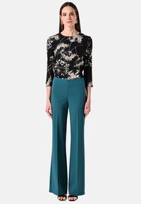 Zwarte bloemen lange mouwtop gecombineerd met hoge taille teal wijde broek, met een gladde textuur en simpele zwarte sandalen.