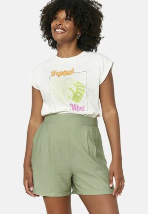 Hellgrüne Shorts mit Falten und hohem Bund, kombiniert mit einem cremfarbenen T-Shirt, das ein grünes Blättergrafik und farbenfrohen Text zeigt.