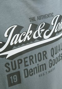 Camiseta de algodón gris con grandes gráficos en blanco y negro que dicen "Jack & Jones", "CALIDAD SUPERIOR" y "Artículos de Denim".
