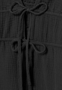 Gros plan d’un tissu foncé et texturé avec deux nœuds noués en cordons doux et épais sur un vêtement.