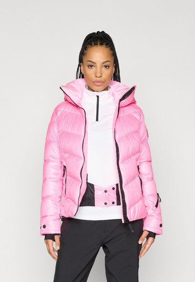 Ροζ φουφό κο jacket με κουκούλα, με επενδυμένο σχέδιο και μαύρες λεπτομέρειες. Συνδυασμένο με λευκή μπλούζα με ψηλό λαιμό και μαύρο παντελόνι.