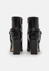 Czarne skórzane botki za kostkę z zaokrąglonym noskiem, średniej wysokości obcasem typu słupek, zamkiem błyskawicznym z boku oraz ozdobnym paskiem z klamrą na zewnętrznej stronie.