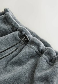 Szürke polár rövidnadrág, rugalmas derékkal, fekete zsinórral és finom textúrával. Közeli képen a varrás részletei.