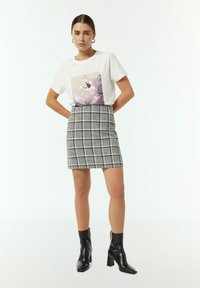 Witte t-shirt met een grafische print, gecombineerd met een zwart-wit geruite mini-jurk. Zwarte enkellaarzen maken de outfit compleet.
