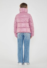 Giacca a vento rosa lucido con colletto alto, texture a coste e cuciture orizzontali, abbinata a jeans blu larghi e sneakers bianche.