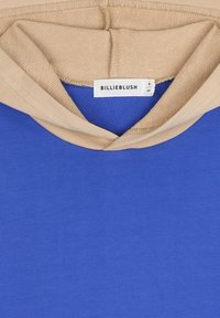 Felpa blu con cappuccio beige, caratterizzata da una texture liscia e un'etichetta che legge "BILLIEBLUSH." Include un design semplice senza pattern.