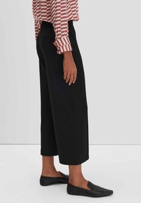 Culotte-stijl zwarte broek van zachte stof, met een wijde pijp en een elastische tailleband, gecombineerd met platte zwarte schoenen.