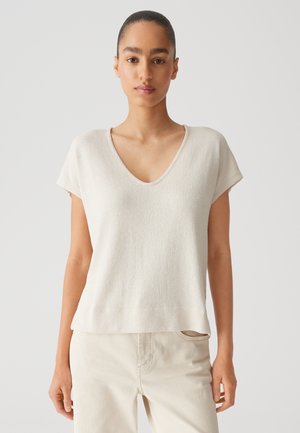 Top corto a maniche corte color beige chiaro con scollo a V in tessuto strutturato e vestibilità comoda, abbinato a pantaloni beige chiaro.