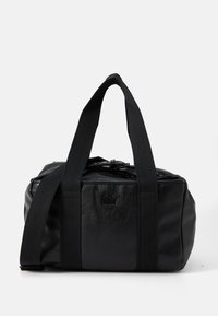 Black leather duffel bag with a structured shape. Features black textile handles and a top zip closure. Subtle logo on the front.