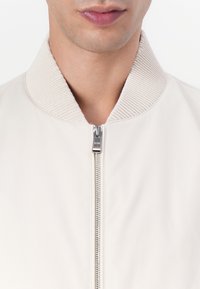 Light beige bomber jacket with a textured corduroy collar, featuring a front zipper and smooth fabric, emphasizing a minimalist design.