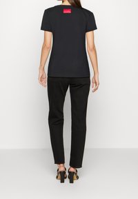 Černé bavlněné tričko s kulatým výstřihem, se červenou vyšívanou nášivkou na zádech. V kombinaci s černými úzkými kalhotami a sandály na podpatku.