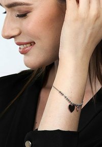 Bracciale con perline in tono argento, due ciondoli a forma di cuore—uno nero e uno argento—su una delicata catena, indossato su un polso.