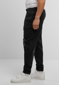 Sorte sweatpants med en strækbar talje, sidelommer og slim fit. De har grå detaljer langs de ydre ben og en blød tekstur.