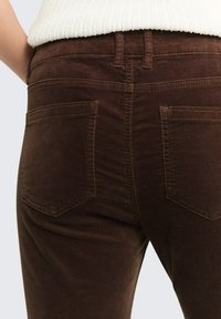 Bruine corduroy broek met twee achterzakken, gestructureerde stof en stiksels. Hooggelegde taille met riemlussen.
