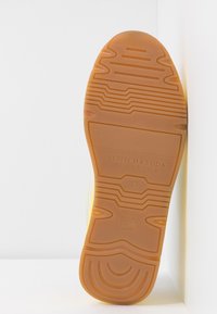 Yellow sneaker sole with textured rubber, featuring pronounced tread patterns, embossed brand name, and size indication.