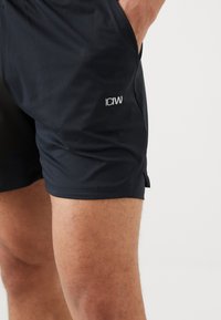 Svarte treningsshorts laget av lett stoff, med nettingtekstur og en liten hvit logo på siden.