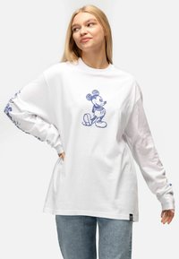 Maglietta bianca a maniche lunghe con una schizzo blu di Topolino sul davanti e motivi decorativi blu sulle maniche. Design dalla vestibilità casual.