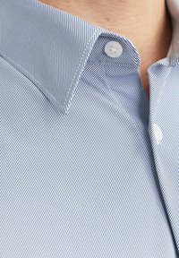 Camicia con bottoni caratterizzata da un pattern a righe blu e bianche, con colletto a punta e bottoni bianchi, realizzata in tessuto di cotone morbido.