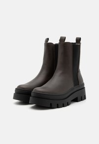 Bottes de cheville en cuir marron avec des panneaux élastiques sur les côtés, semelles épaisses noires et languettes à l'arrière pour un enfilage facile.