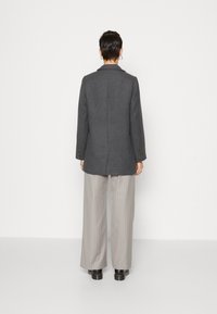 Grauer Wollmischung-Blazer mit Reverskragen, geradem Schnitt, Schlitz auf der Rückseite und Knopf-Akzenten an den Ärmeln. Kombiniert mit hell gestreiften Hosen.