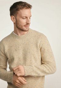 Beżowy sweter w robótkach z okrągłym dekoltem, z drobnymi plamkami w kolorze pomarańczowym i niebieskim, żebrowanymi mankietami o wyraźnej fakturze oraz luźnym krojem.