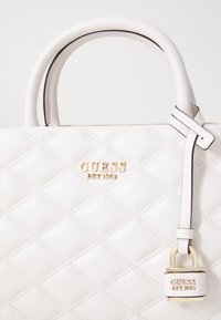 Biała pikowana torba wykonana z gładkiej sztucznej skóry, z złotym logo i niewielkim detalem w postaci kłódki. Teksturowana powierzchnia z diamentowym przeszyciem.