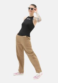 Top nero senza maniche con logo, pantaloni beige a gamba larga e sneakers rosa. Accessoriato con occhiali da sole neri. Sfondo bianco semplice.