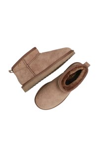 Botines de ante color beige con forro de piel suave, punta redonda y suela corta y plana. Presentan una costura decorativa y una lengüeta en la parte posterior.